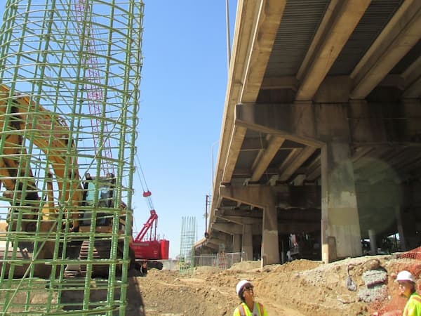 Construction activity beneath an elevated section of I-95 in Philadelphia, with crews, equipment, and rebar cages visible on site. Part of the ongoing I-95 Section GIR reconstruction project supported by Dawood Engineering.