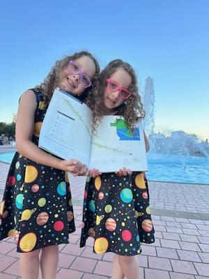 twin girls in planet glasses holding esri mapbook in front of fountain